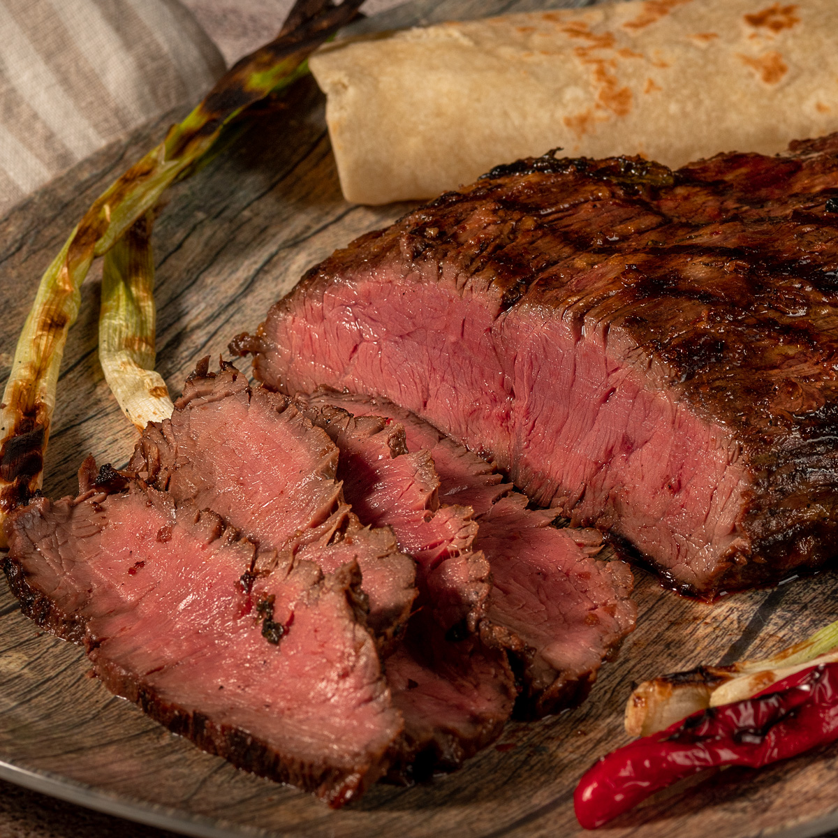 Grilled carne asada steak on a plate with warm flour tortillas and grilled onions.