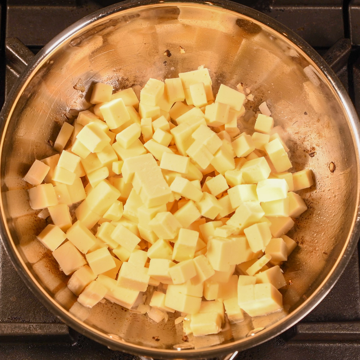Add cubed American cheese to the onion and garlic mixture.
