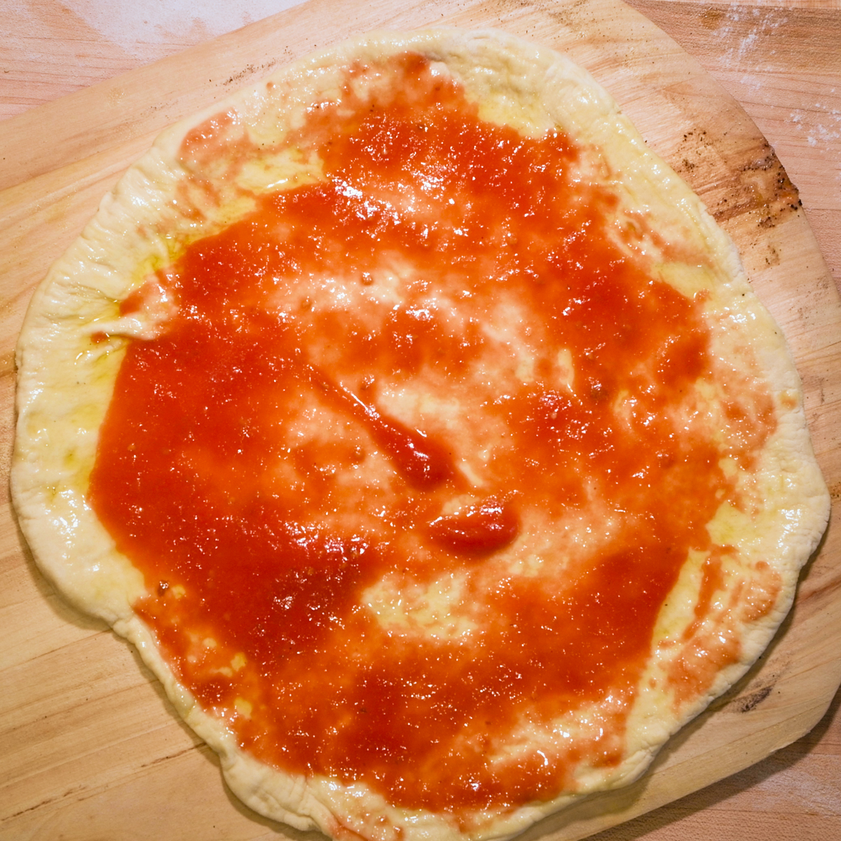 Add sauce to piza dough.