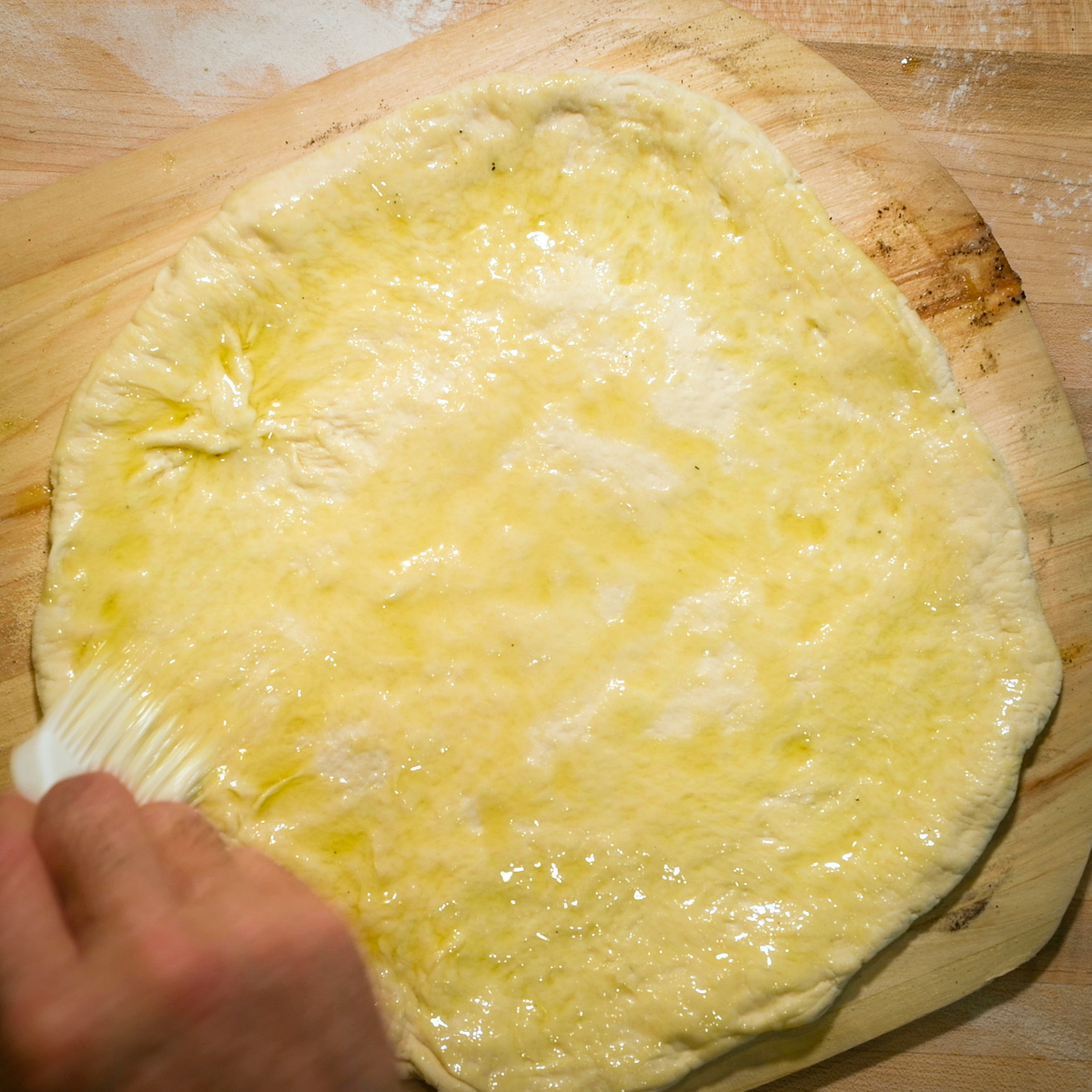 Spread olive oil on pizza dough.
