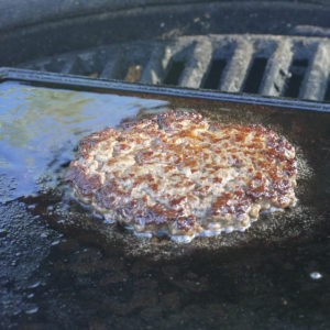 Hamburger cooking in beef tallow on a cast-iron griddle inside a Kamado Joe.