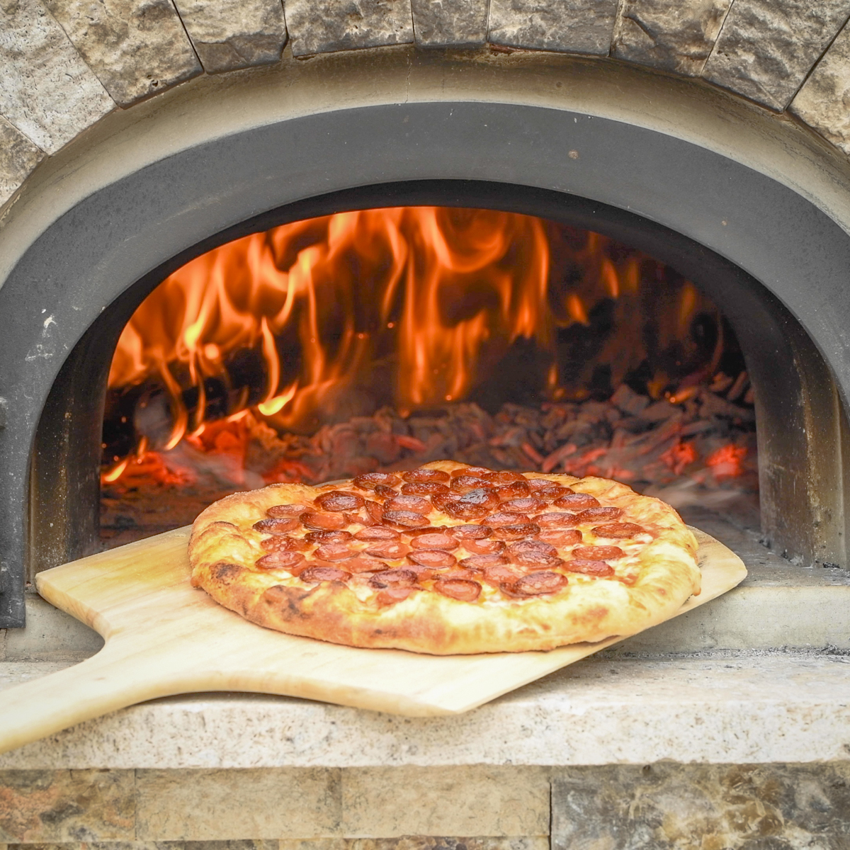 Cooked pepperoni pizza coming out of a wood-fired ovfen.