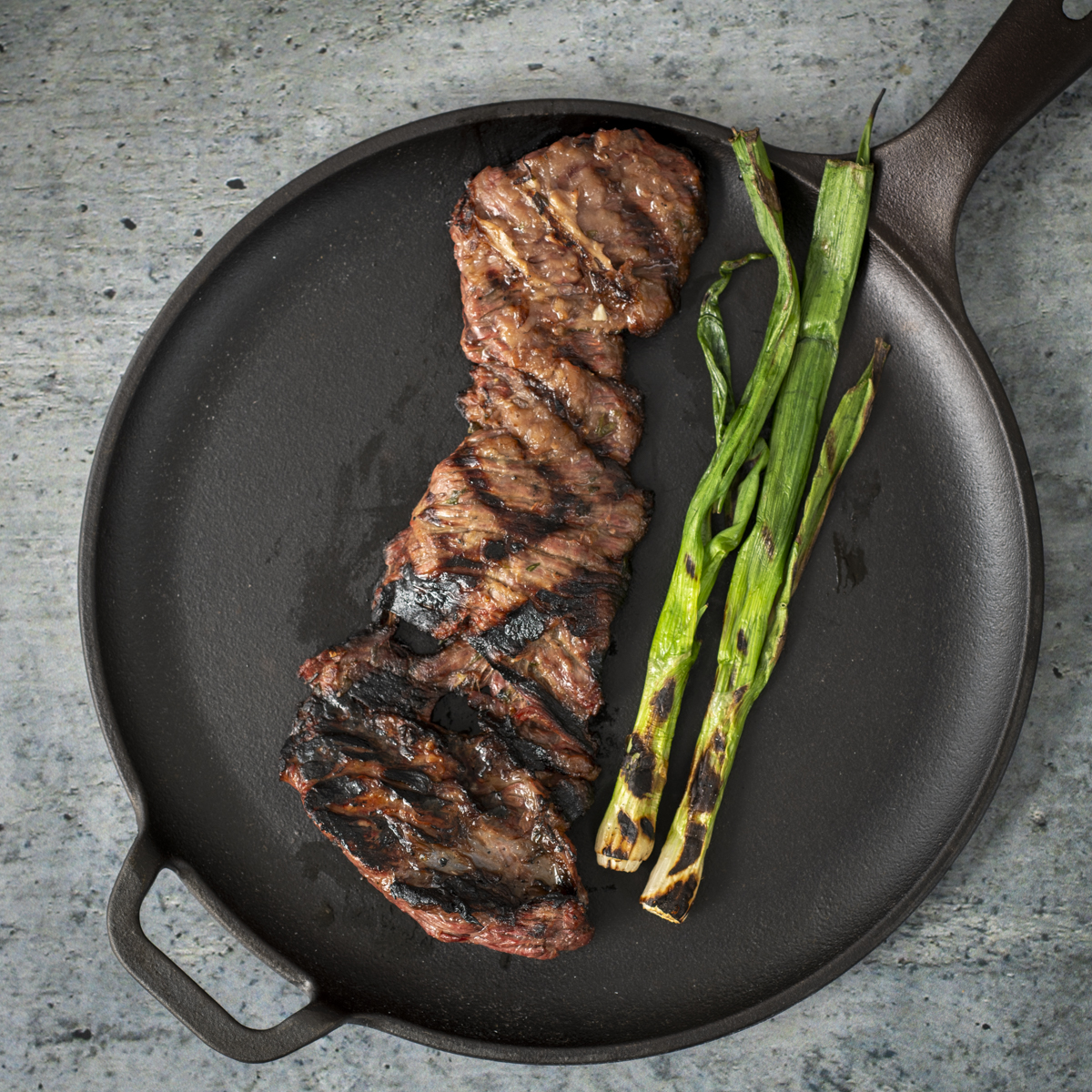 Grilled skirt steak and a green onion on a cast-iron comal.