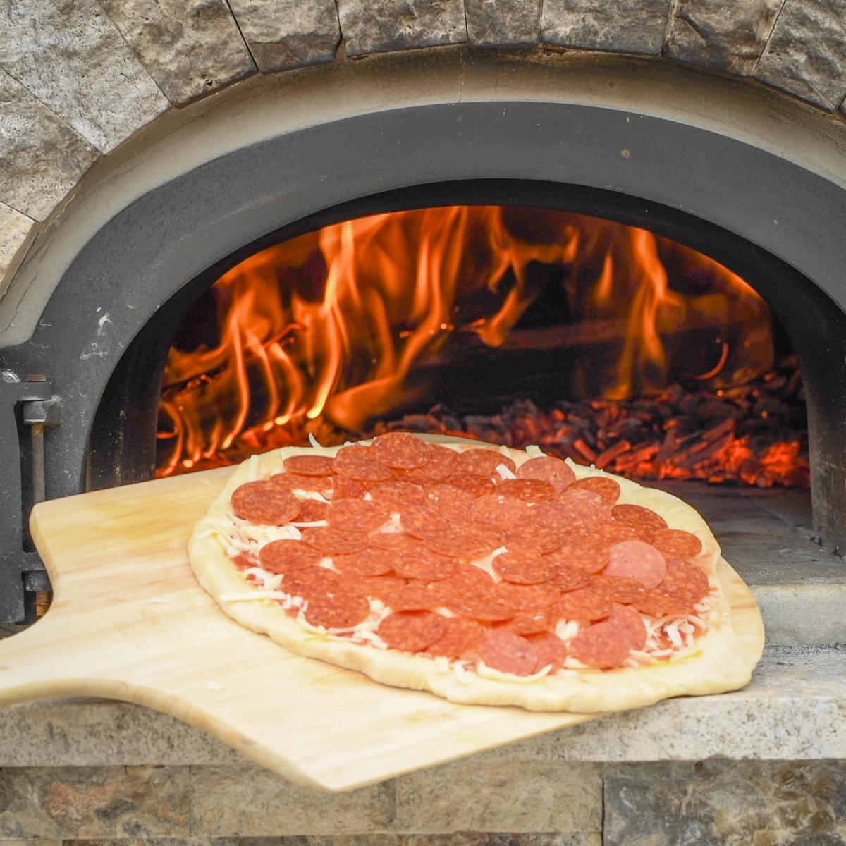 Pepperoni pizza going into a wood-fired oven.