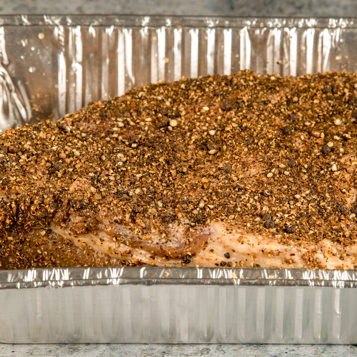 Season the brined brisket and place it in a foil tray.