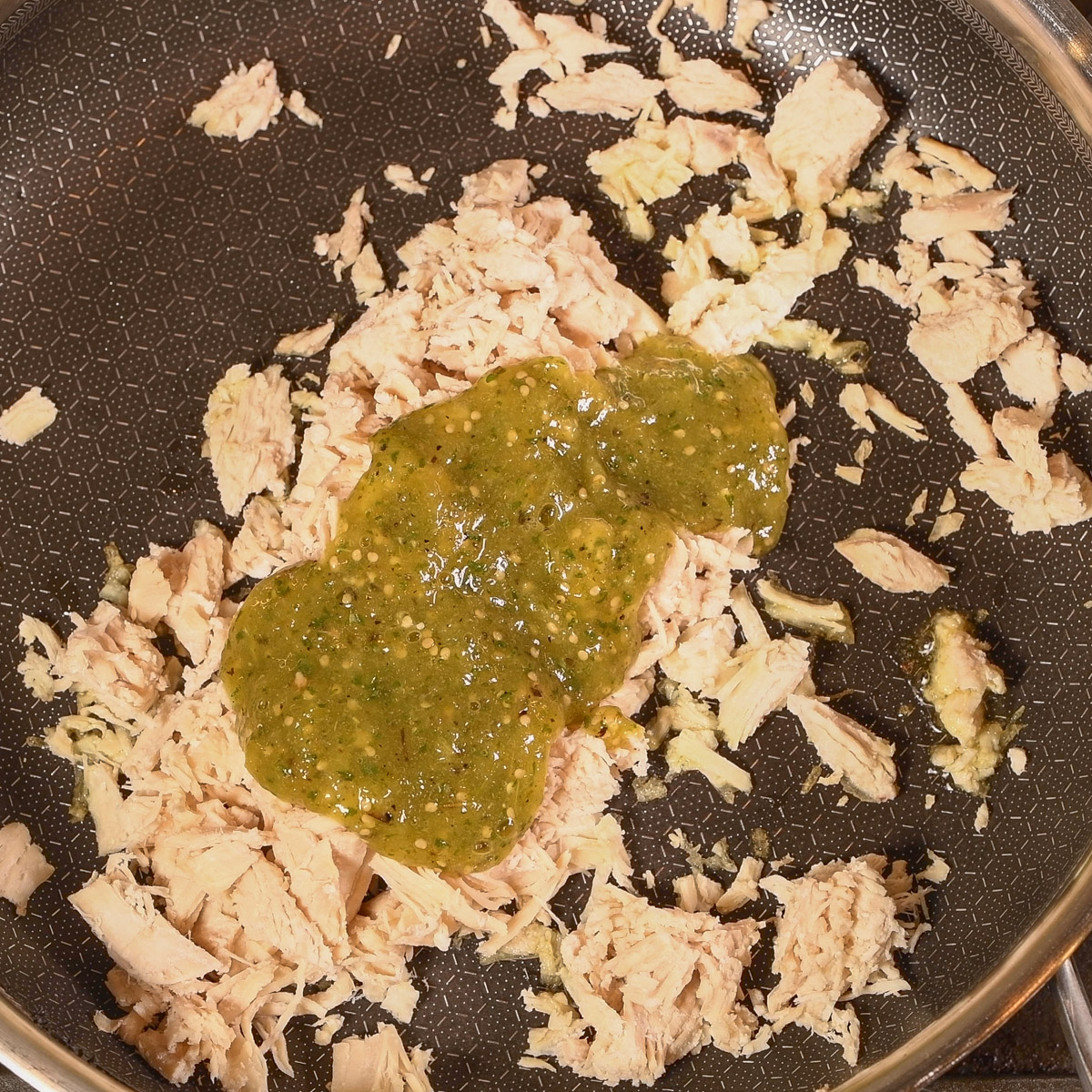 Chicken in a hot skillet with salsa verde.