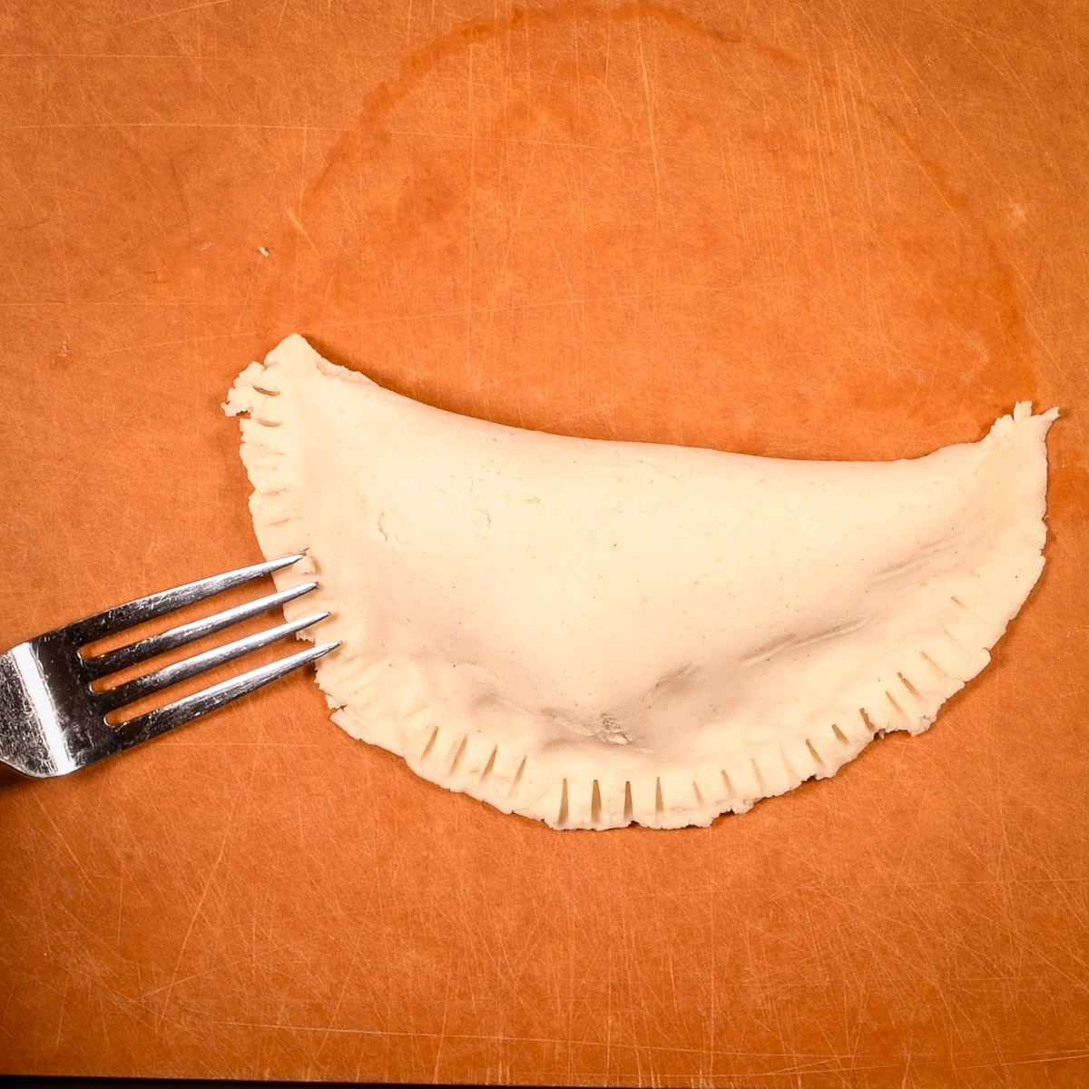 Fold the empanada dough over and seal with the tines of a fork.